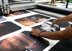 Person arranging glossy photo proofs on a print table, adjusting a black-and-white image with their hands in a studio setting.